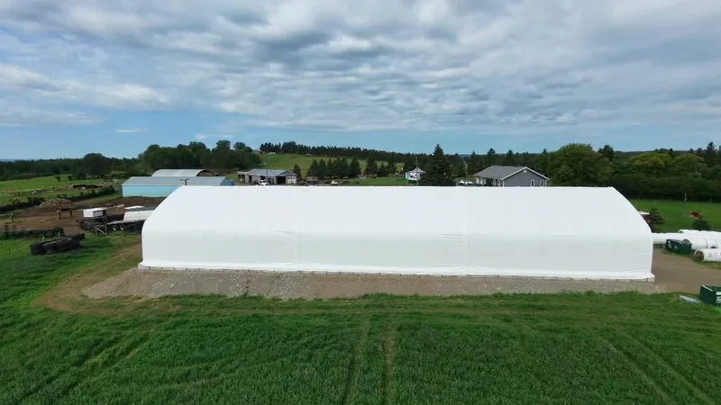 Aerial side view of a long white fabric building in its farm setting
